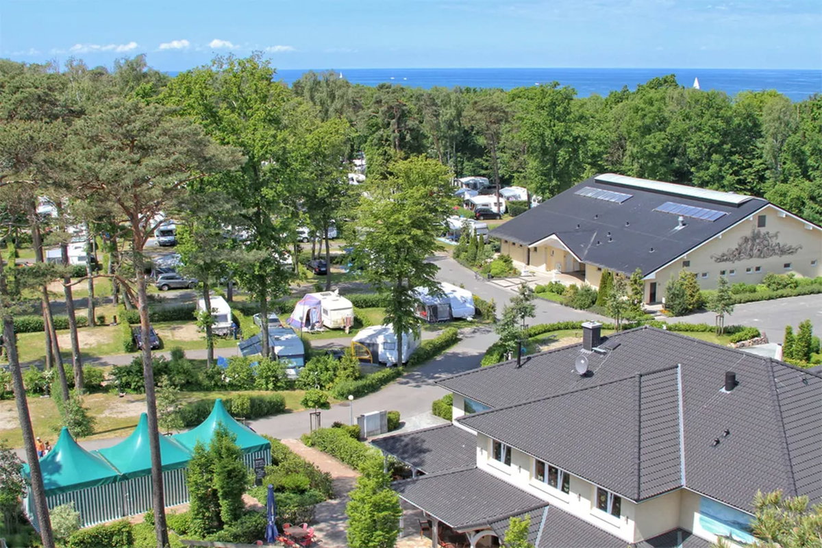 Camping.info nr 1 w Niemczech: Kemping Kühlungsborn. Możesz zobaczyć widok z lotu ptaka na kemping na wsi, z morzem w tle.
